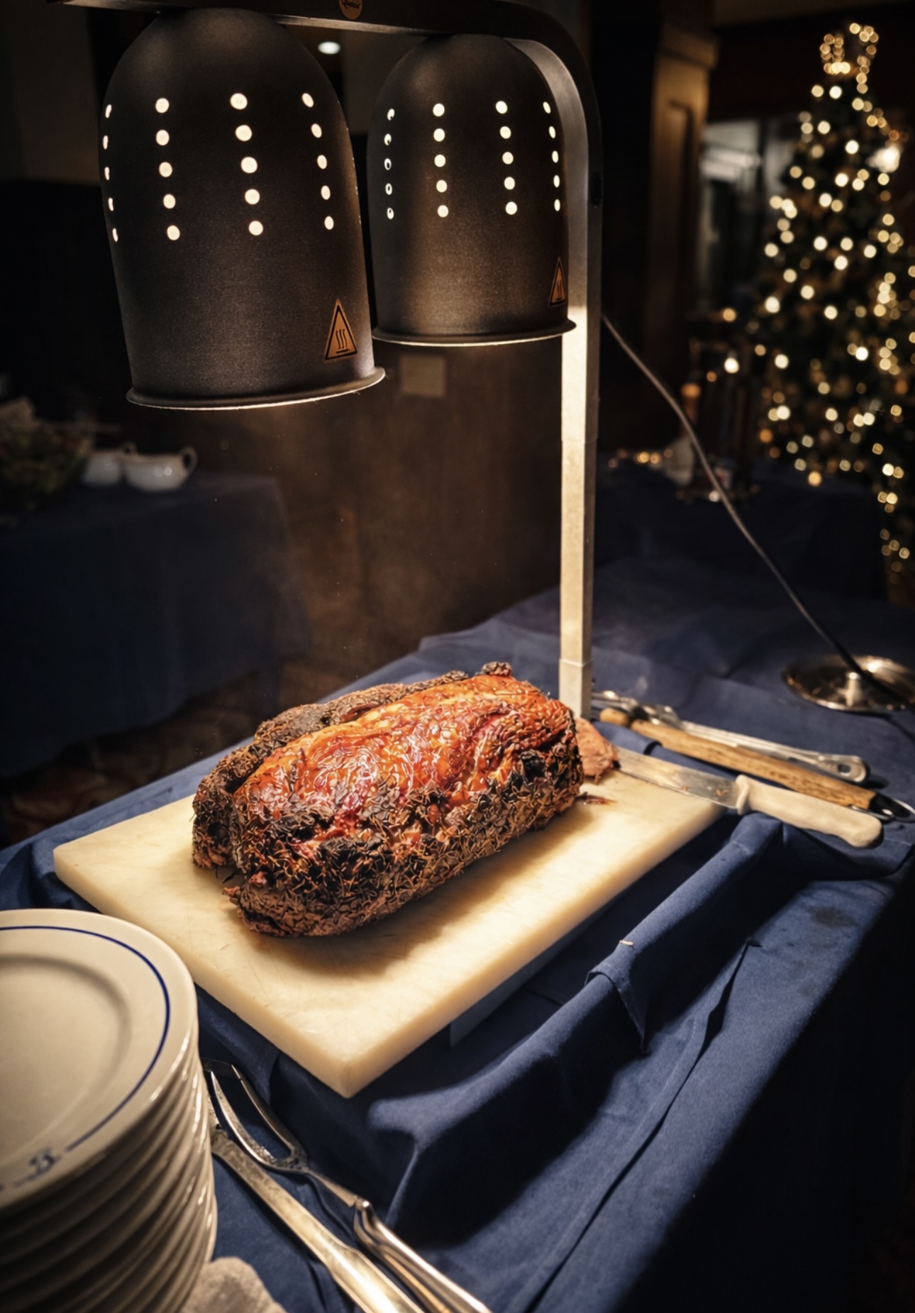Herb-crusted roast carving station under warming lamps with Christmas tree backdrop