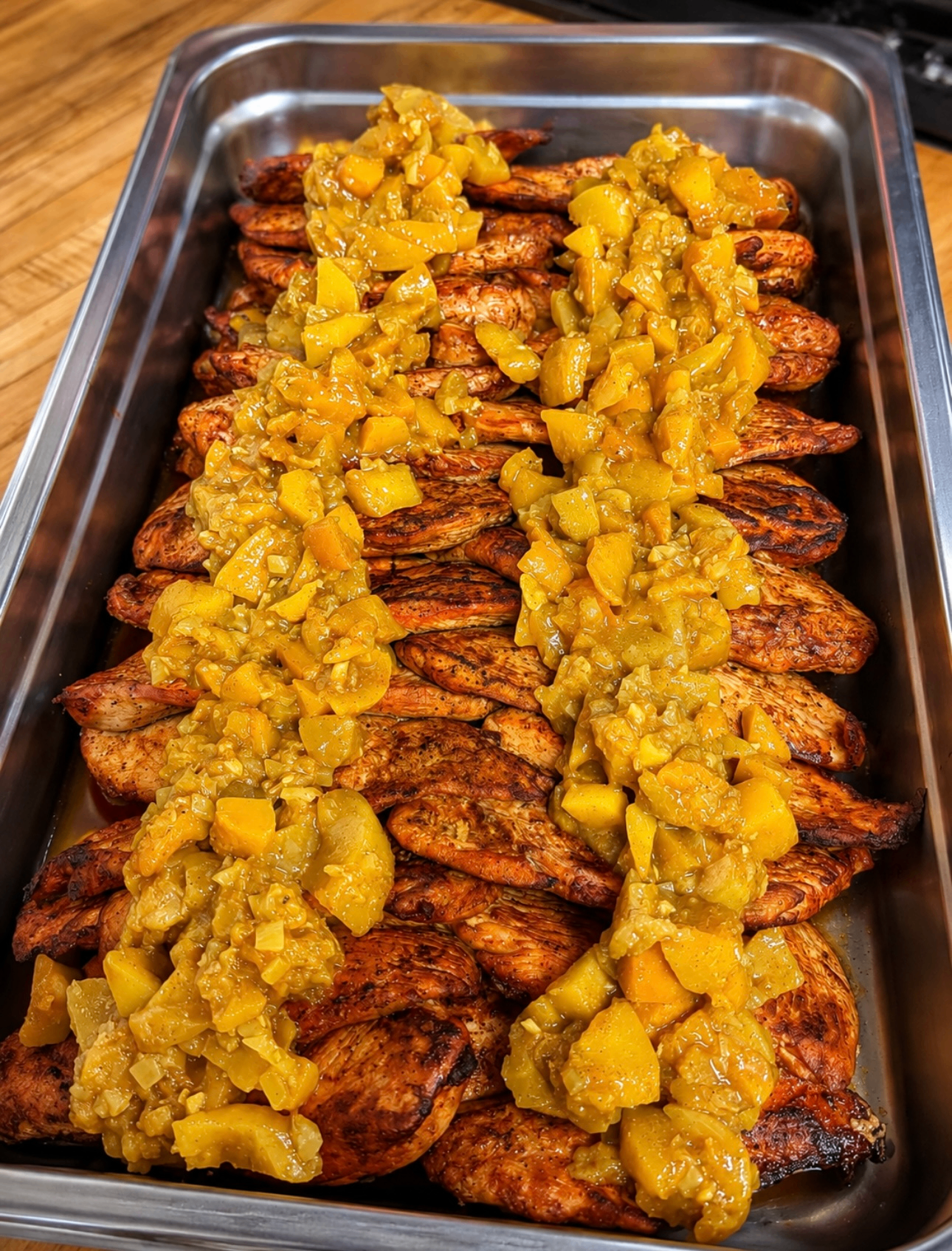 Catered tray of prepared chicken with bright yellow topping