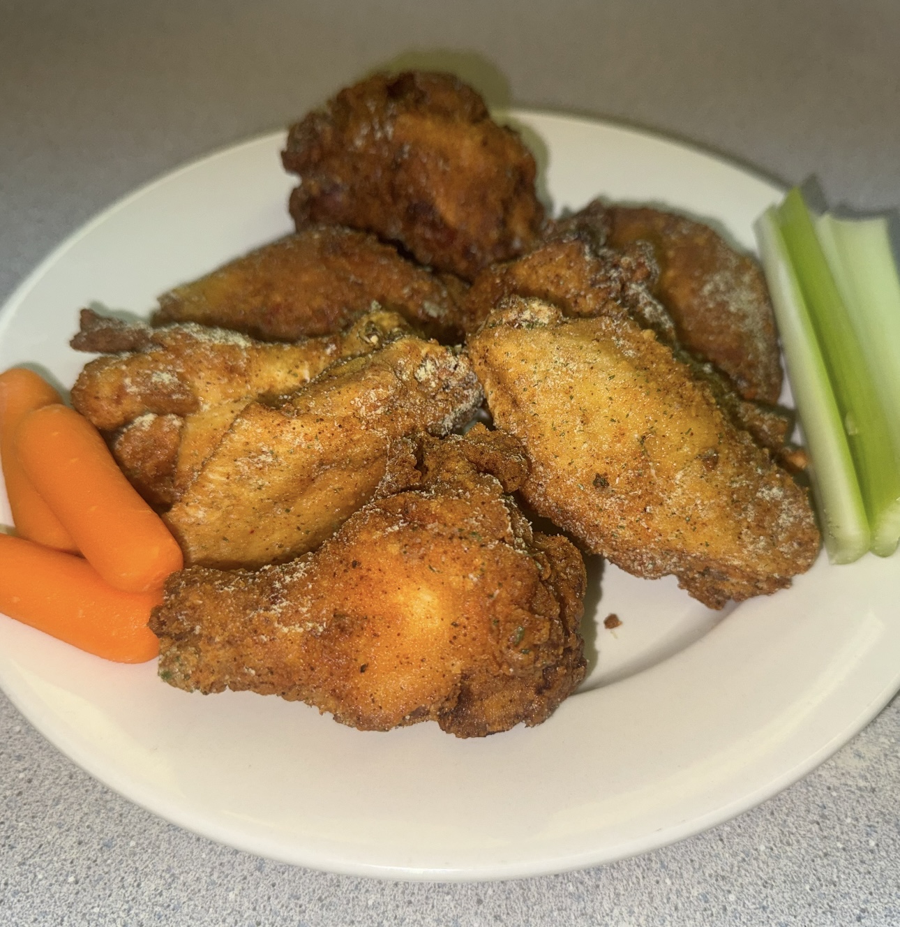 Crispy seasoned fried chicken wings plated with carrots and celery