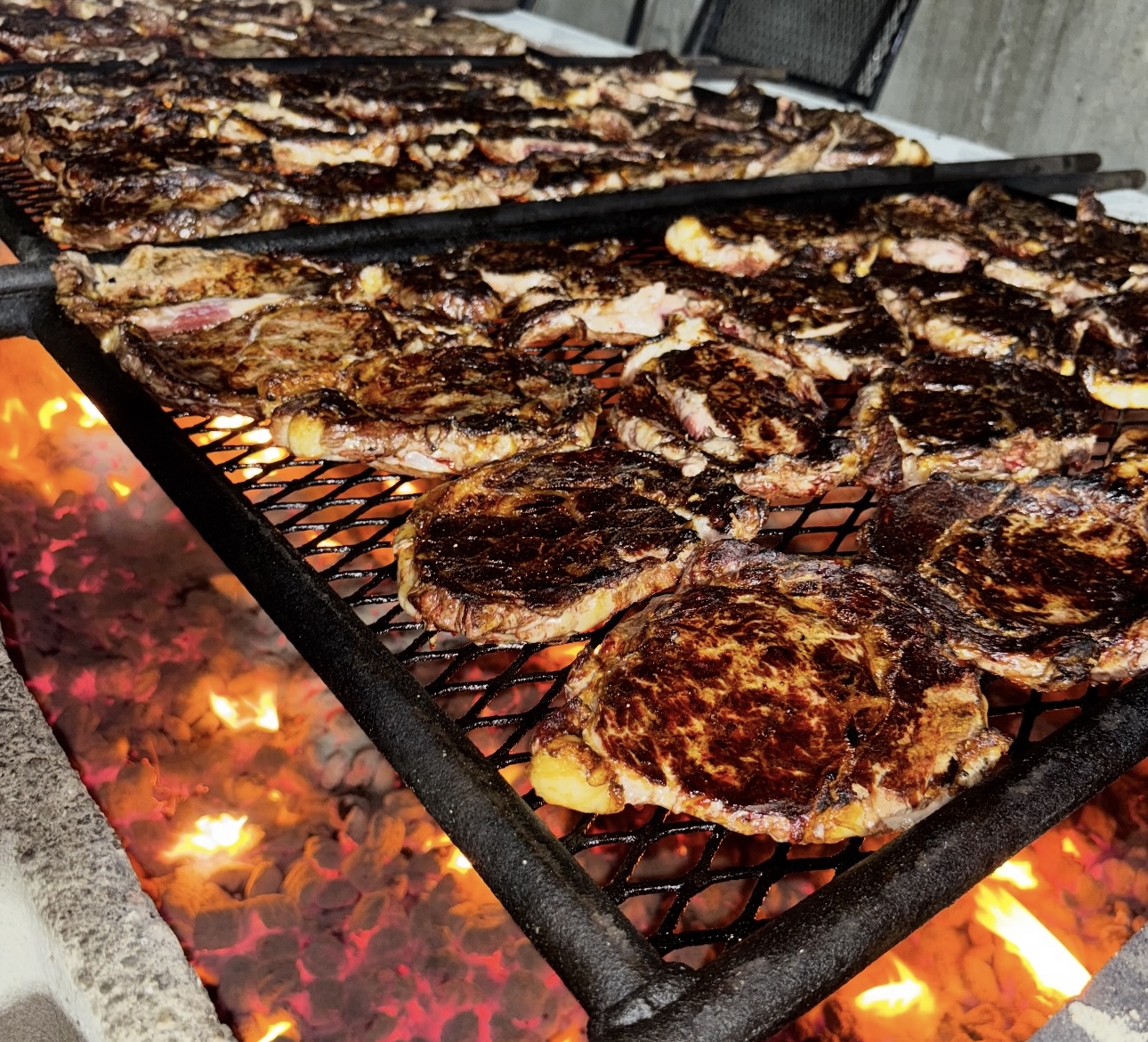 Ribeye steaks searing over open flame on a wood-fired grill