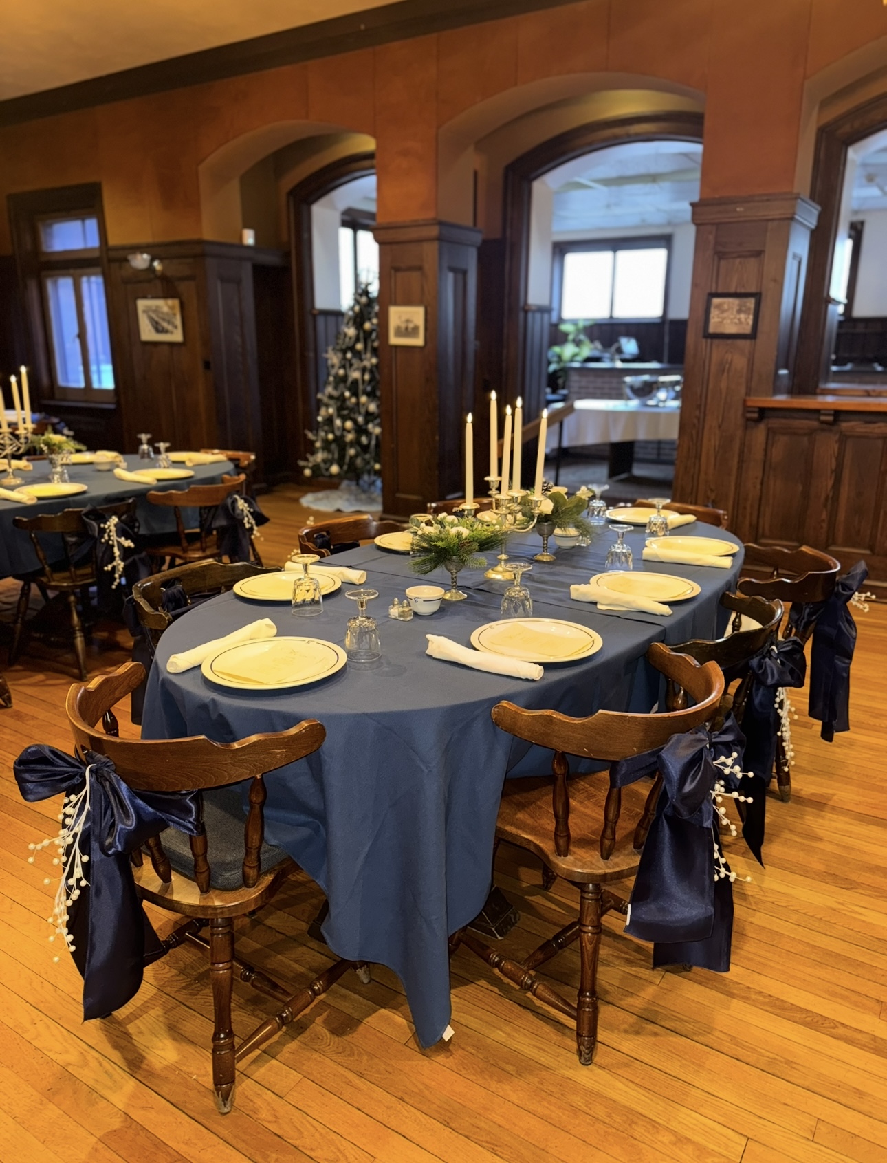 Holiday dining setup with navy linens, candles, and ribbon-tied chairs